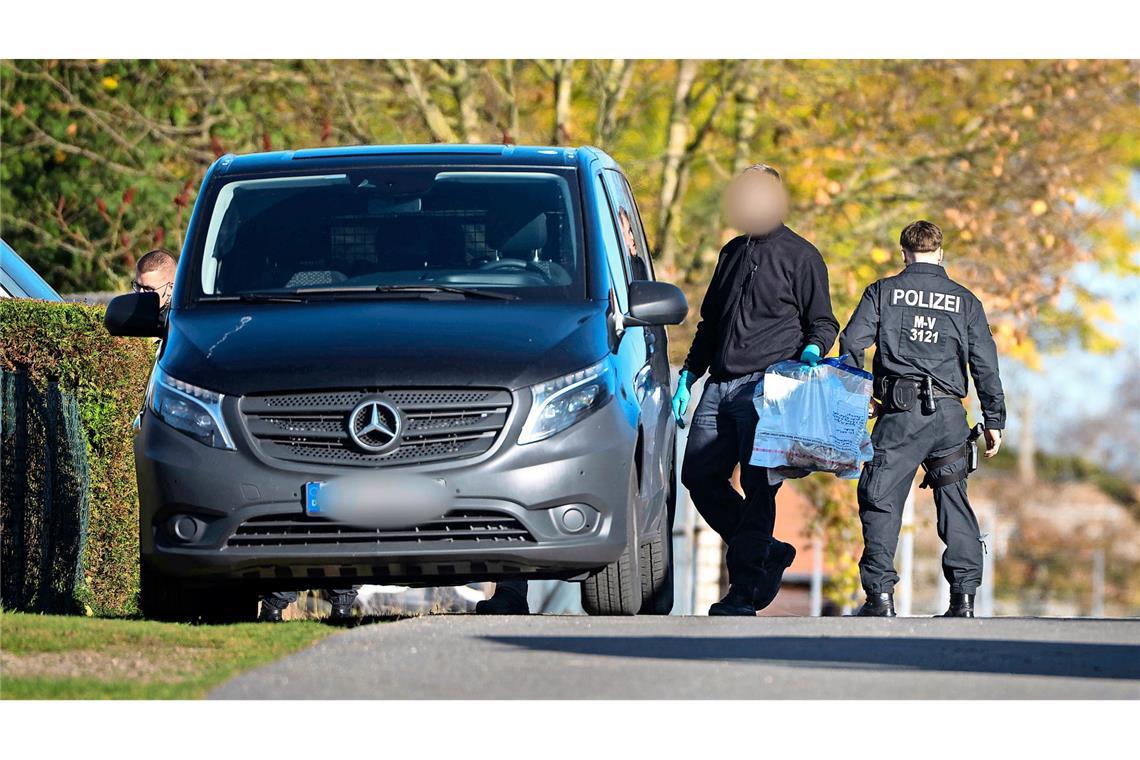 06.11.2025, Mecklenburg-Vorpommern, Güstrow: Ein Ermittler trägt bei einer Hausdurchsuchung in Reimershagen Plastiktüten mit Sportschuhen über die Straße.
