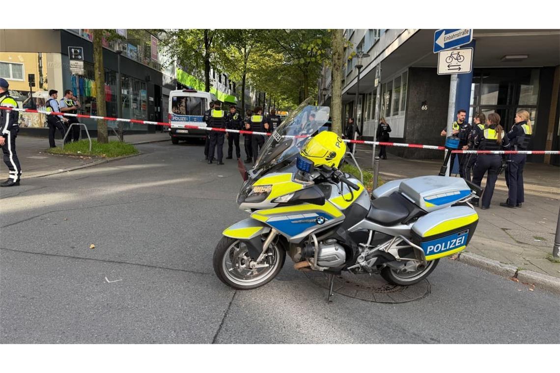 Absperrband hinter einem Polizeimotorrad in der Nähe eines Tatorts. Einsatzkräfte stehen auf einem Parkplatz. Zwei Unbekannte haben mitten in Essen zwei Justizbeamte angegriffen und einen 34 Jahre alten Häftling befreit.