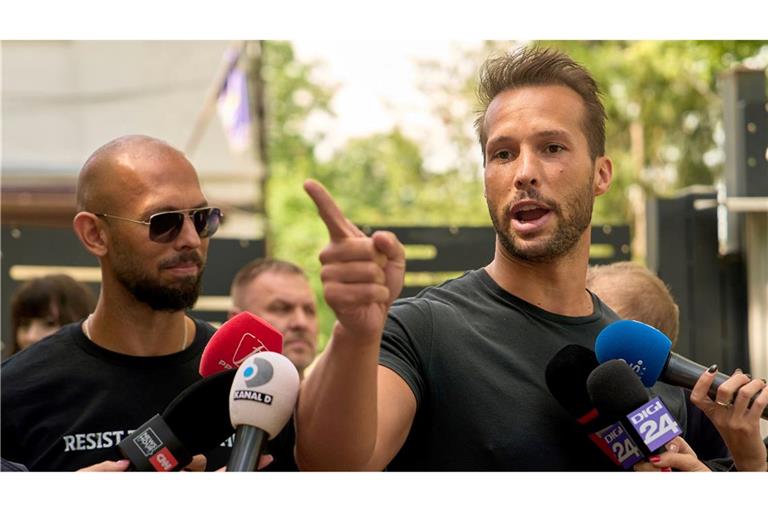 Andrew Tate (links) schaut zu seinem Bruder Tristan Tate, der am 21. Mai vor einer Polizeistation in Voluntari in Rumänien redete.
