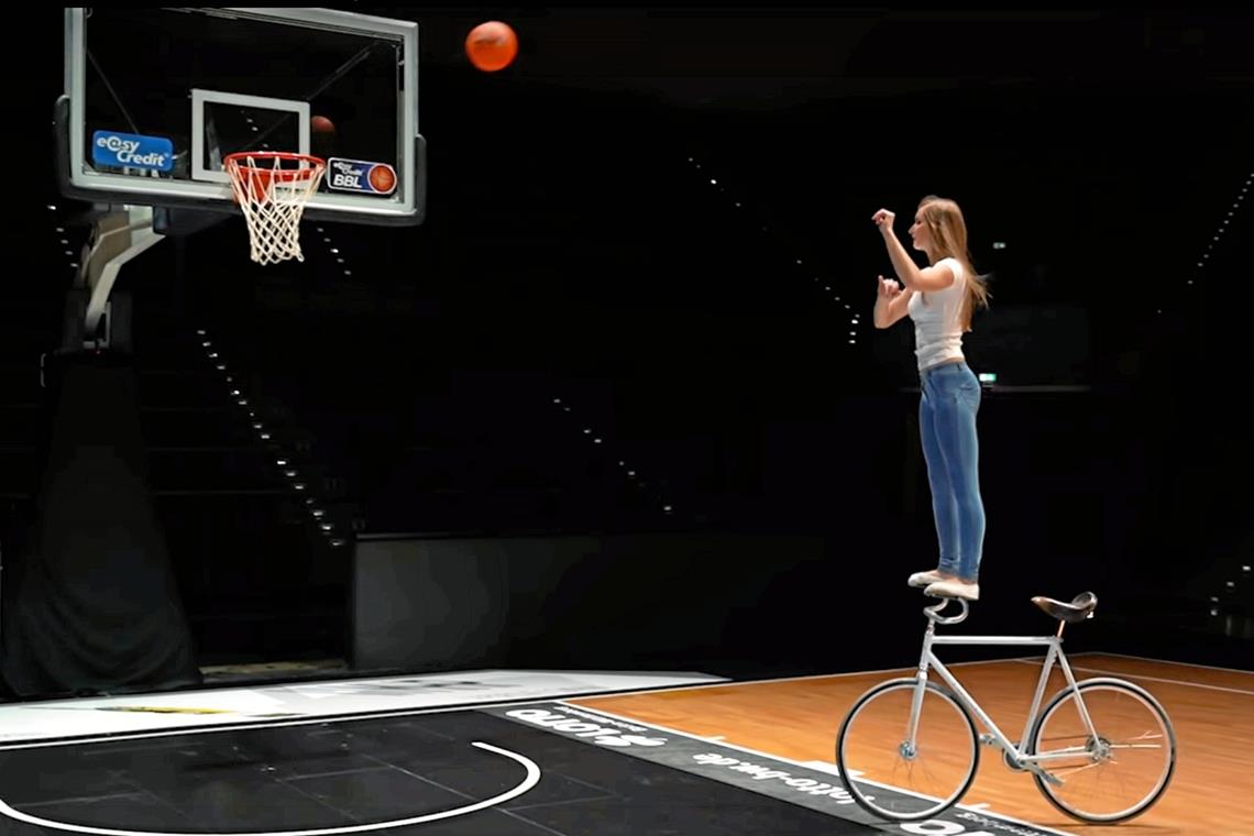 Viola Brand und ihr Wahnsinn mit der NBA Auf dem Kunstrad stehend auf Korbjagd: Viola Brand, die Bestandteil der virtuellen Halbzeitshow zweier NBA-Klubs ist. Screenshot: violalovescycling