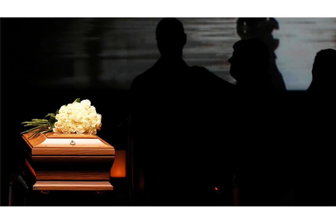 Auf dem Sarg liegt ein Strauß weißer Rosen.