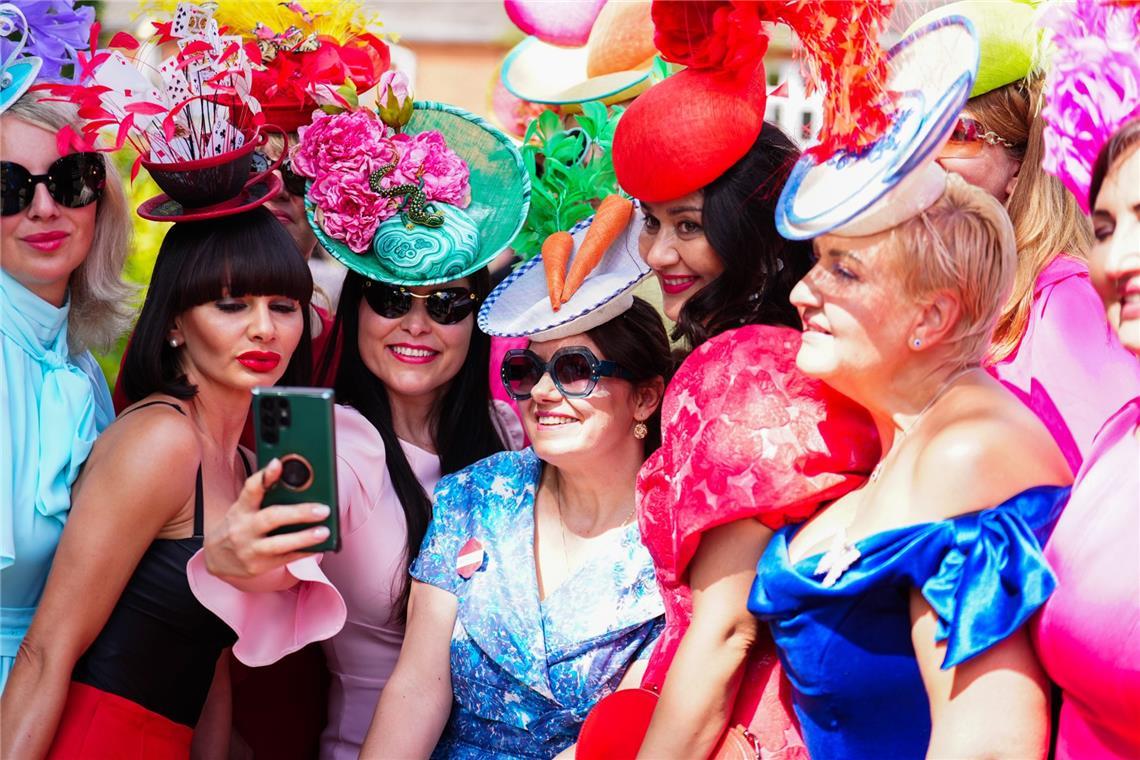 Bei Royal Ascot wird Kopfschmuck zur Hauptattraktion: Die Besucherinnen tragen Hüte und Fascinators in kräftigen Farben, mit Spielkarten, Federn, Blüten, Schleiern und skulpturalen Formen. Dazu dominieren farbintensive Kleider in Pink, Rot, Blau und Pastelltönen.