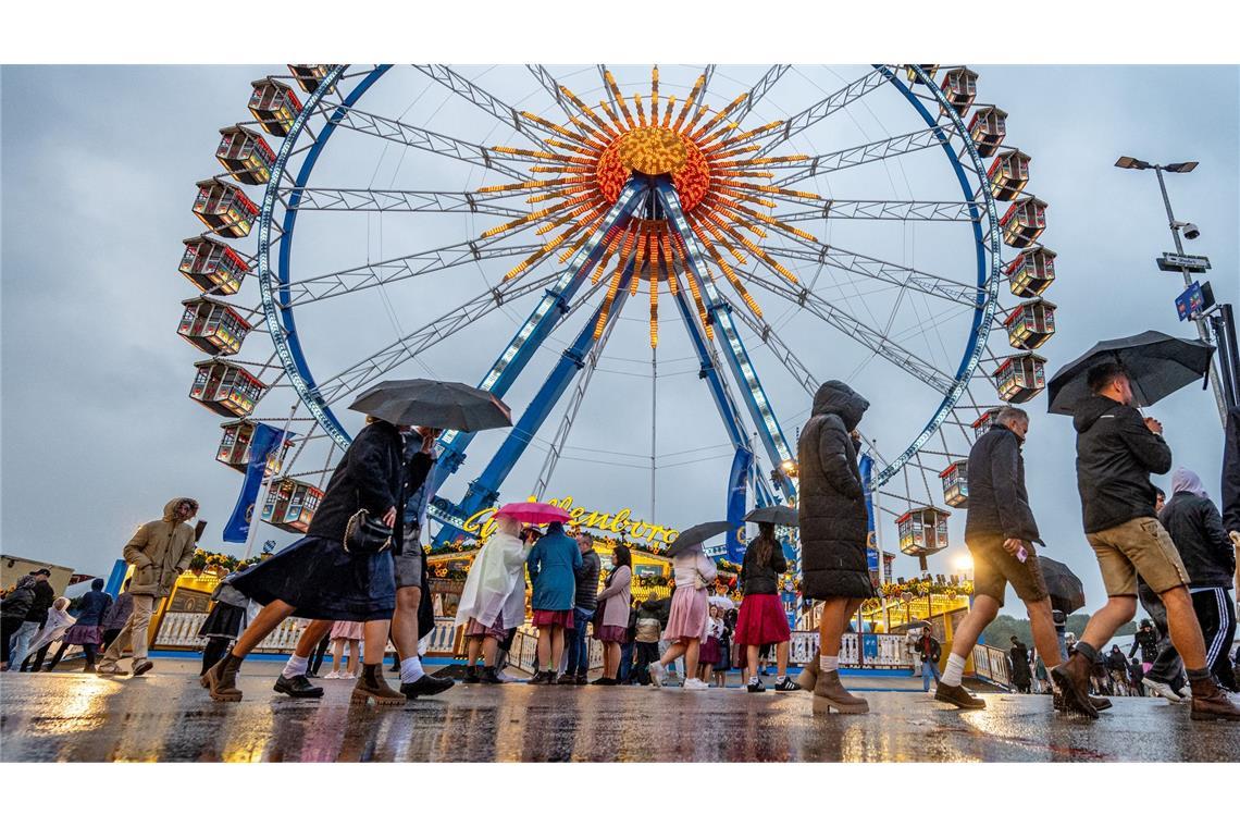 Bilder des Tages Besucher des Oktoberfestes in München gehen im Regen über das Festgelände vor dem Riesenrad.