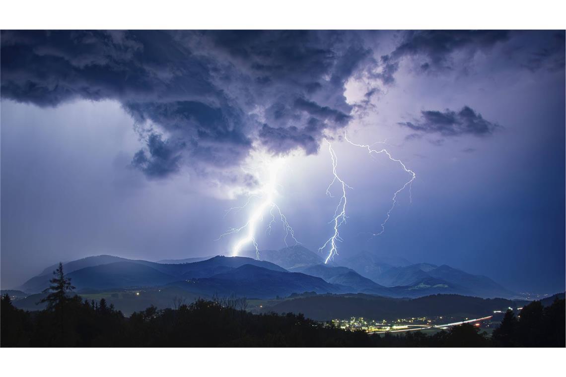 Blitze erhellen den Abendhoimmel bei einem heftigen Gewitter über Siegsdorf und dem Hochfelln in Chiemgauer Alpen in Bayern.