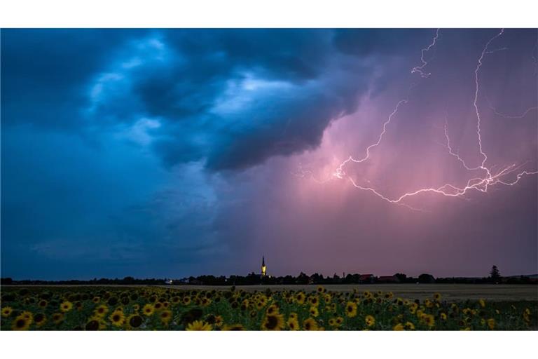 Blitze zucken am Abend über Wechmar mit der Dorfkirche Sankt Viti (Mi.) während Gewitter über Teile von Thüringen ziehen (Archivfoto).