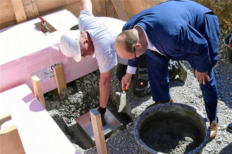 Bürgermeister Armin Mößner (rechts) füllt einige Kellen Betonmischung in den Grundstein mit der Kassette. Foto: Elisabeth Klaper