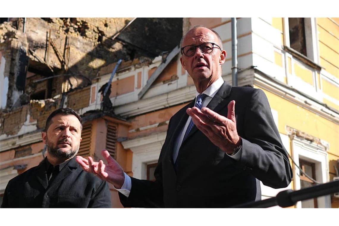 Bundeskanzler Friedrich Merz (r, CDU) und Wolodymyr Selenskyj (l), Präsident der Ukraine,  stehen am zerstörten Gebäude der Nationalen Akademie der Wissenschaften.