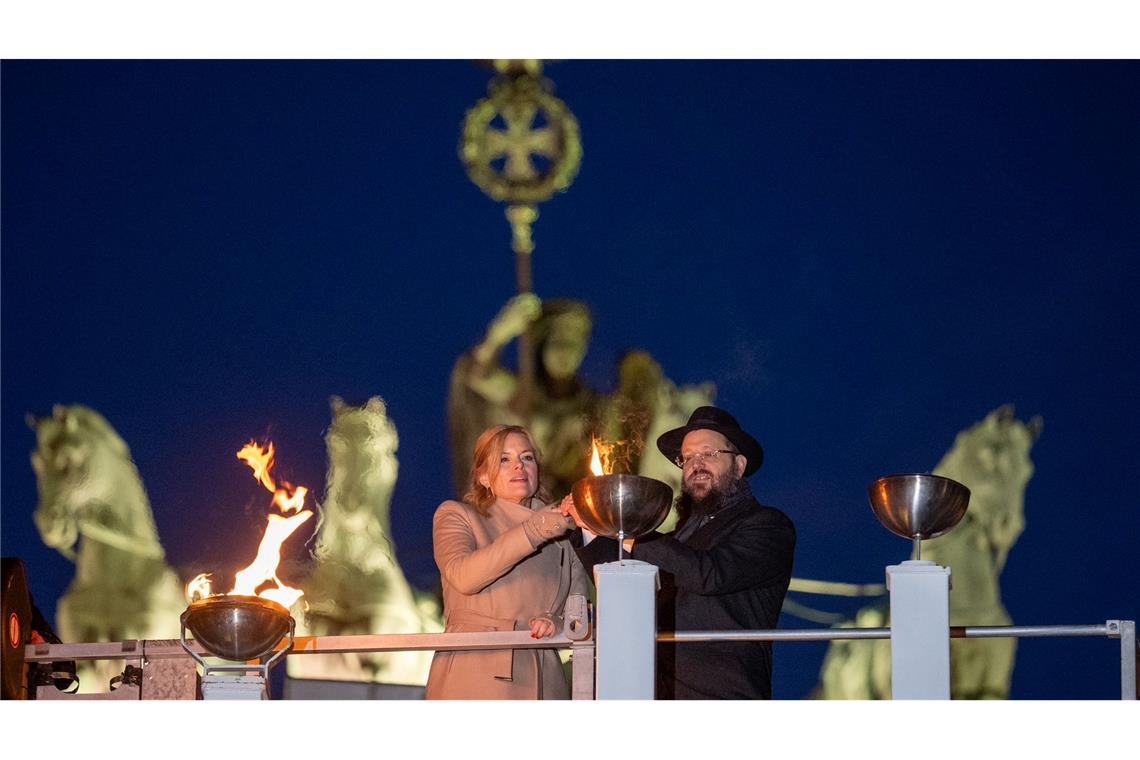 Bundestagspräsidentin Julia Klöckner (CDU) und Rabbiner Yehudi Teichtal entzünden am Brandenburger Tor während einer festlichen Zeremonie die Lichter am Chanukka-Leuchter mittels einer Fackel.