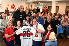 Das Team mit Heimleiterin Alexandra Zieffle (vorne, Zweite von rechts) nimmt das besondere Präsent von Hansi Müller fürs Haus entgegen – ein Trikot für die Einrichtung. Foto: Erich-Schumm-Stiftung