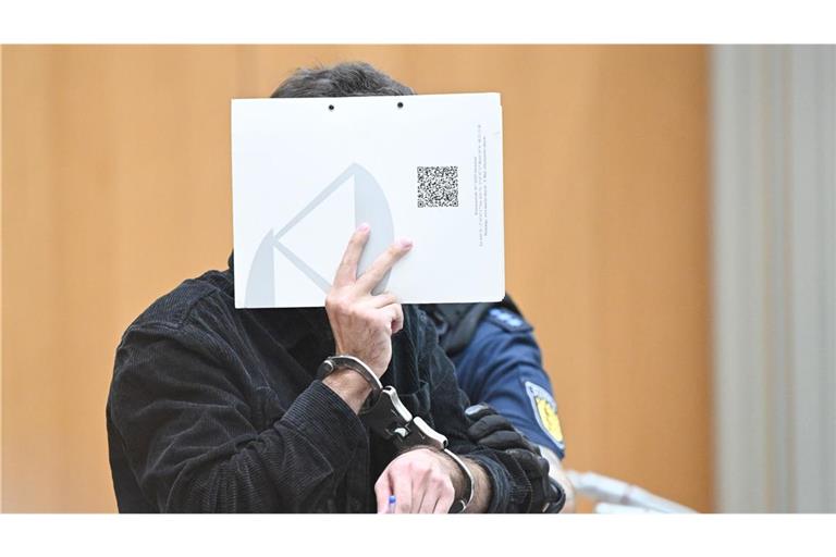 Der Angeklagte  steht zu Beginn eines Verhandlungstages mit einem Aktenordner vor dem Gesicht im Gerichtssaal (Archivbild).