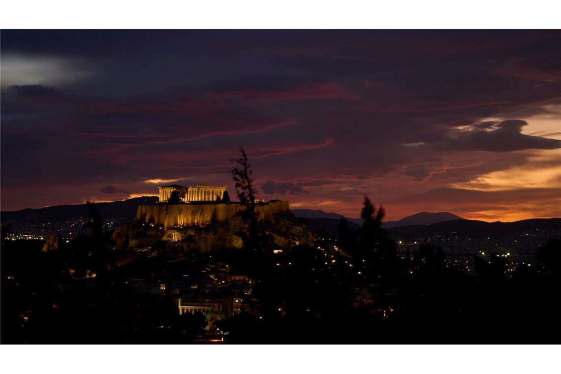 Der antike Parthenon-Tempel auf dem Akropolis-Hügel in Athen wird in der Abenddämmerung an einem bewölkten Tag beleuchtet.