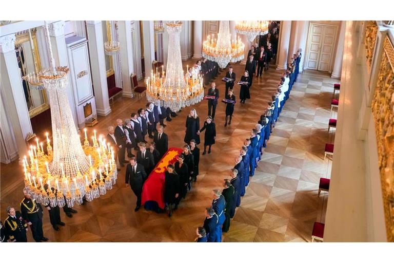 Der Sarg von König Harald V. wird am 31. August 2026 von Mitgliedern der königlichen Familie vom Roten Salon in die Palastkapelle in Oslo überführt. Hinter dem Sarg gehen Königin Mette-Marit von Norwegen und Königin Sonja von Norwegen Hand in Hand.
