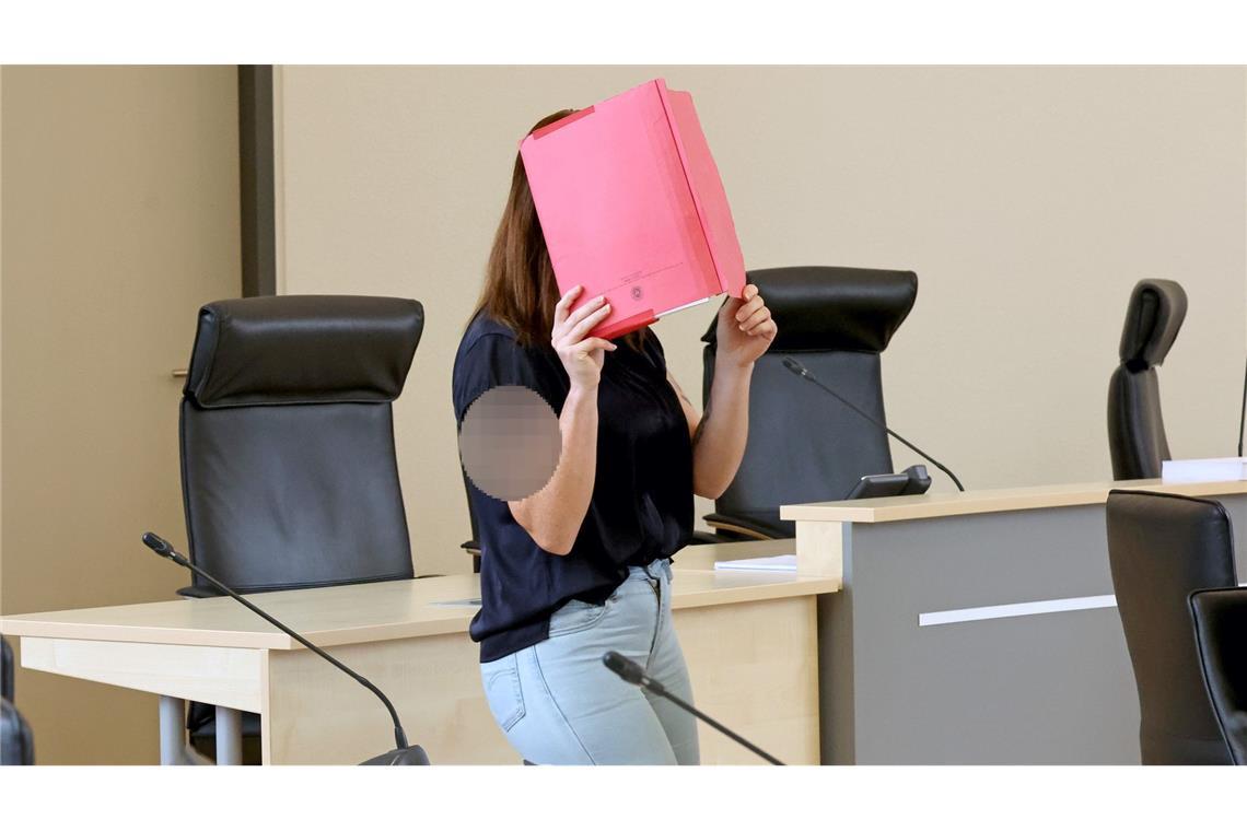 Die Angeklagte betritt den Gerichtssaal mit rotem Aktendeckel vor dem Gesicht.