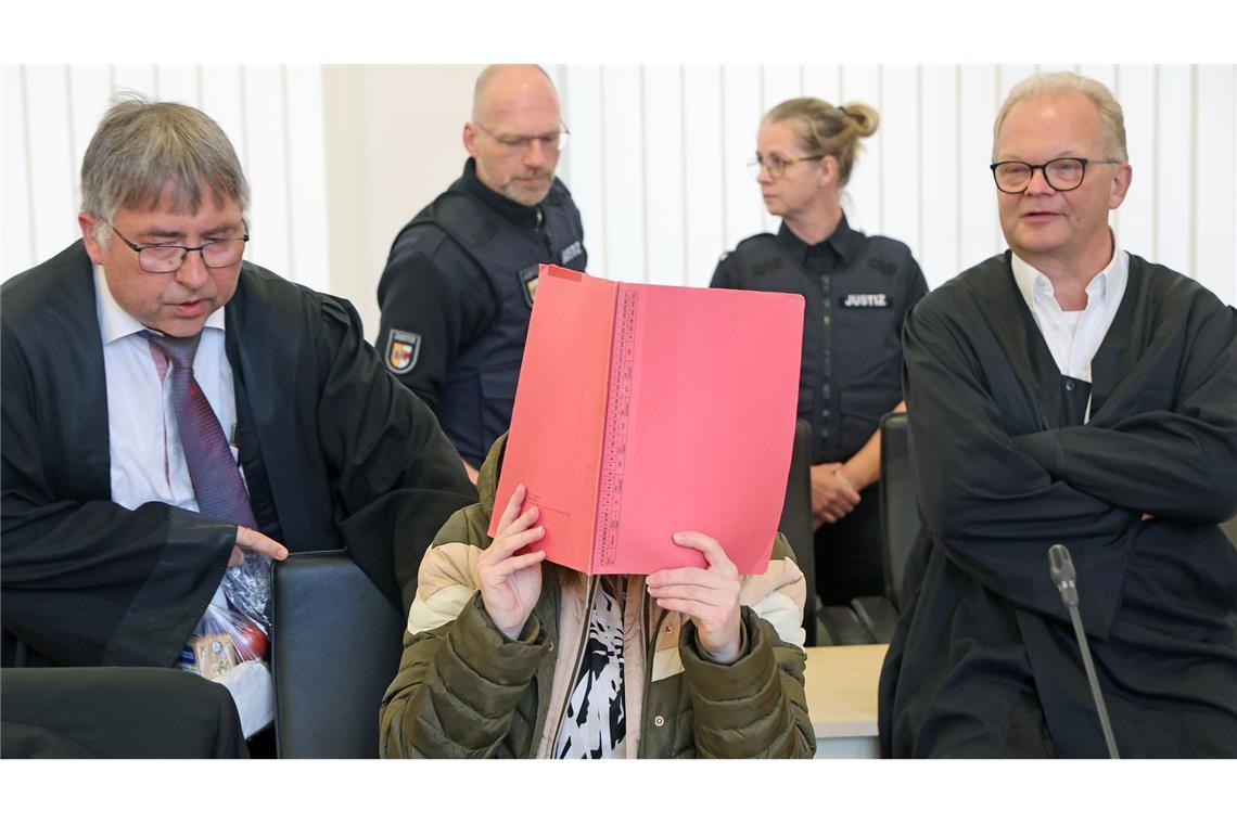 Die Angeklagte sitzt mit Aktendeckel vor dem Gesicht zwischen ihren Verteidigern Andreas Ohm (l-r) und Thomas Löcker.