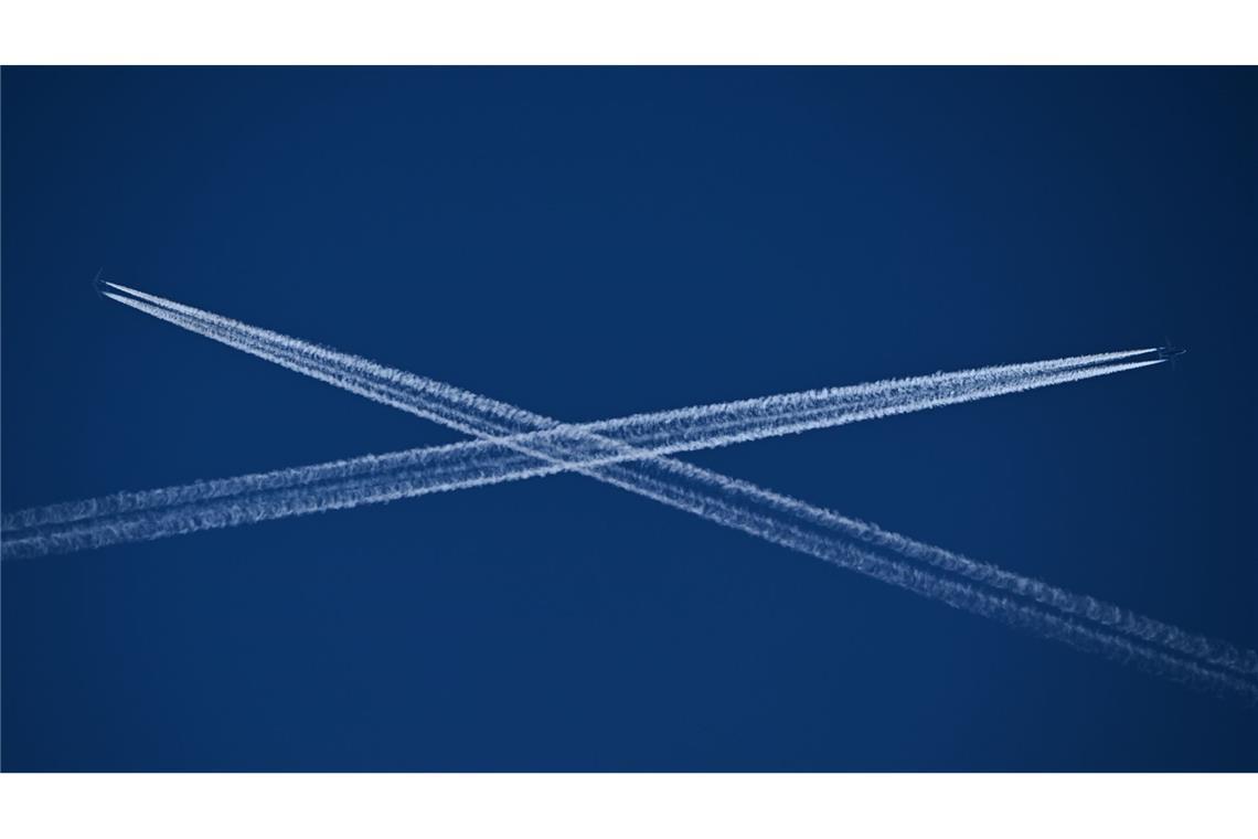 Die Routen zweier Passagiermaschinen, die Kondensstreifen hinter sich herziehen, kreuzen sich am blauen Himmel über Frankfurt am Main.