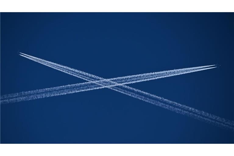 Die Routen zweier Passagiermaschinen, die Kondensstreifen hinter sich herziehen, kreuzen sich am blauen Himmel über Frankfurt am Main.