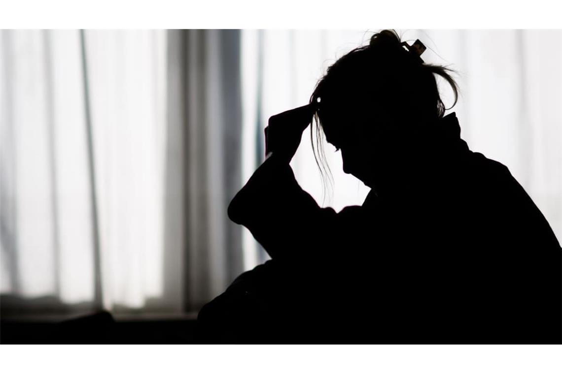 Die Silhouette einer Frau zeichnet sich vor einer hellen Fensterfront ab (gestellte Szene).