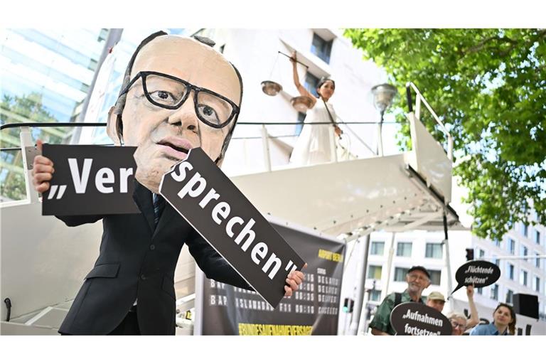 Ein Aktivist mit Merz-Maske zerbricht während einer symbolischen Protestaktion von Kabul Luftbrücke und Campact ein Schild mit der Aufschrift "Versprechen".