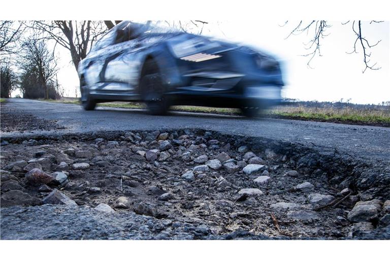 Ein Auto fährt an einem Schlagloch in einer Allee vorbei. Das Frostwetter der letzten Wochen sorgt für kaputte Straßen mit tiefen Schlaglöchern.