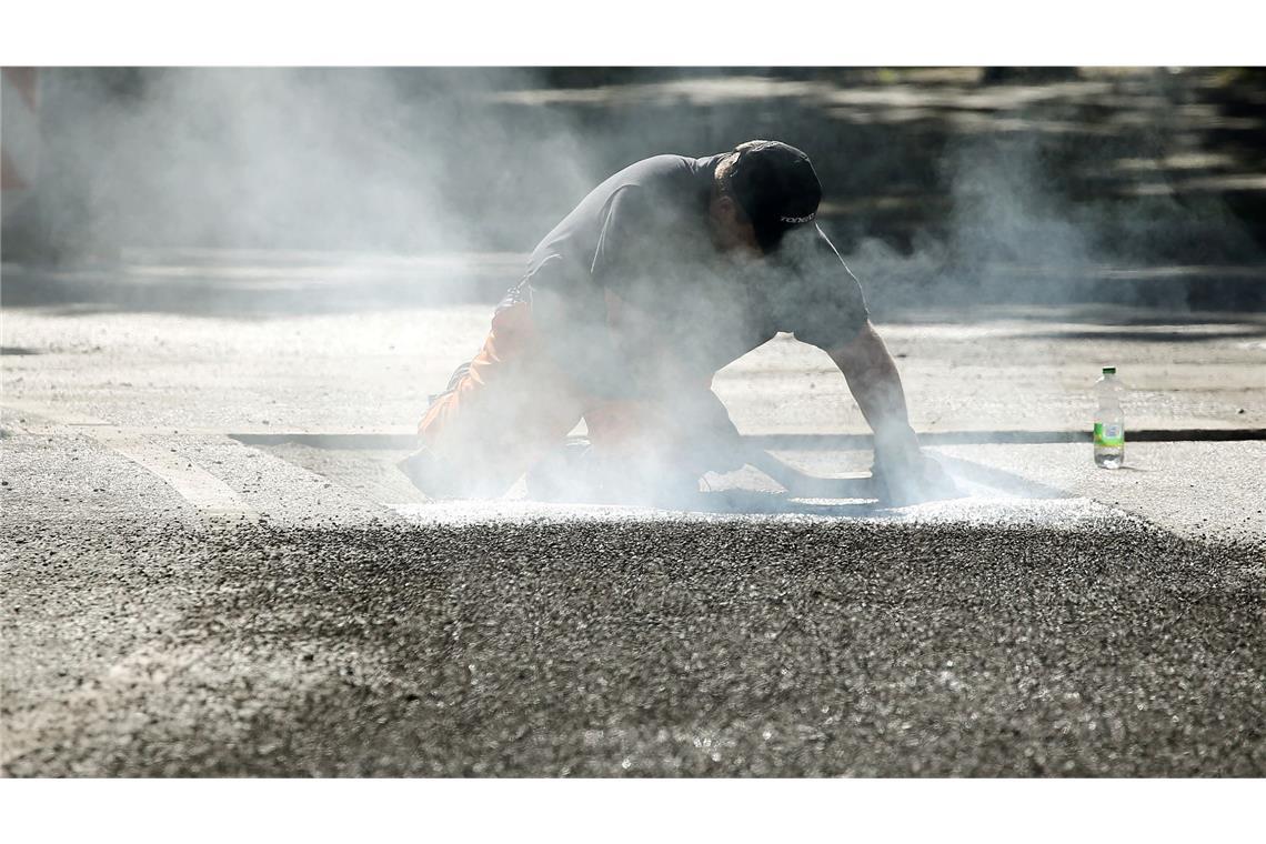Ein Bauarbeiter repariert eine Straße in Berlin mit Bitumen, einem Bindemittel für Asphalt. (Symbolbild)