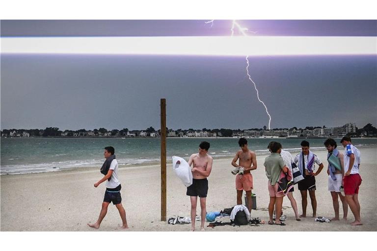 Ein Blitz erhellt den Himmel, während sich Menschen darauf vorbereiten, den Strand während eines Gewitters über der Stadt La Baule im Westen Frankreichs zu verlassen.