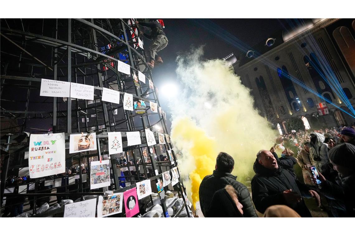 Bilder des Tages Ein Demonstrant befestigt eine georgische Flagge an einem vor dem Parlamentsgebäude aufgestellten künstlichen Weihnachtsbaum.