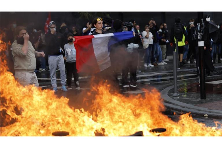 Ein Demonstrant der Protestbewegung «Bloquons Tout» (Alles blockieren) zeigt eine französische Nationalflagge neben brennenden Müllkübeln.