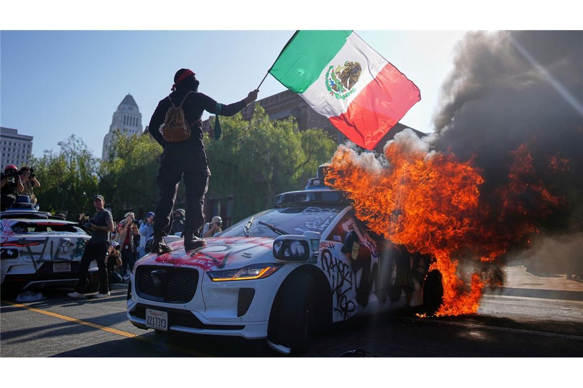 Bilder des Tages Ein Demonstrant steht auf einem brennenden Waymo-Taxi in der Nähe des Metropolitan Detention Center in der Innenstadt von Los Angeles.