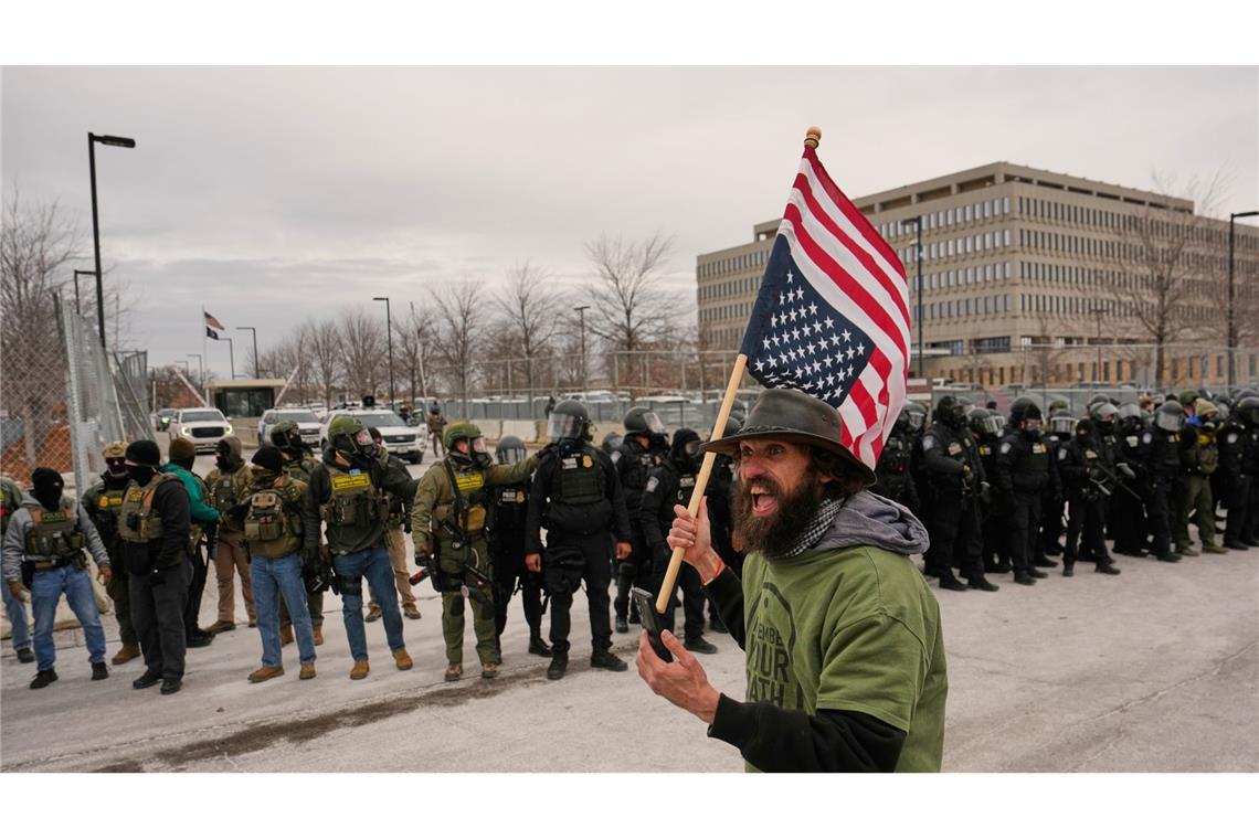 Ein Demonstrant trägt eine umgedrehte US-Fahne vor den Beamten der Einwanderungsbehörde ICE bei einem Protest gegen die Behörde vor dem Bishop Henry Whipple Federal Building.