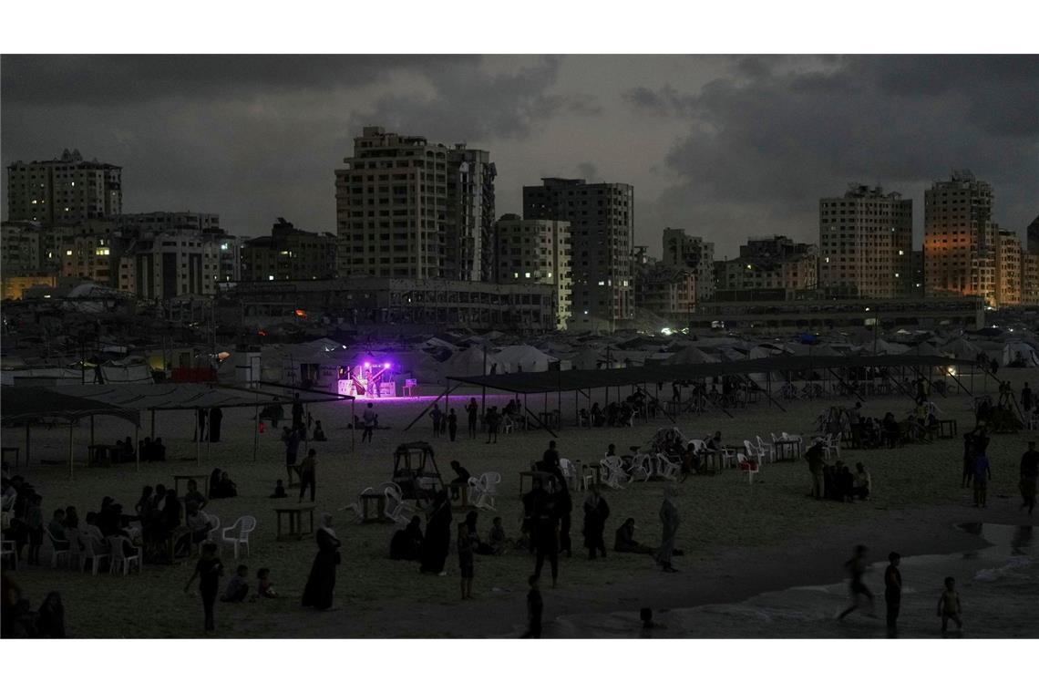 Ein Essensstand leuchtet in der Abenddämmerung, während sich Palästinenser in der Nähe des Hafens von Gaza Stadt im Mittelmeer abkühlen.