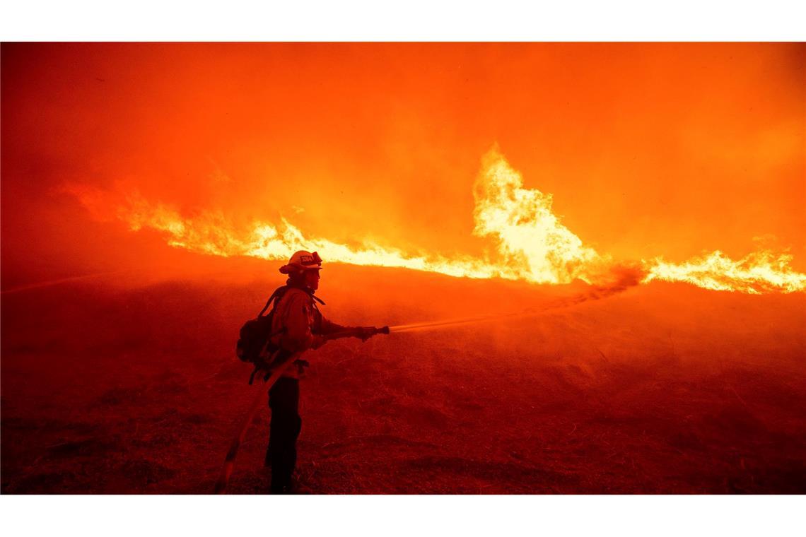 Bilder des Tages Ein Feuerwehrmann versprüht Wasser, während er die vom Hughes-Feuer in Kalifornien verursachten Flammen an einem Straßenrand überwacht.