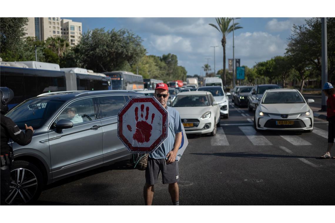 Ein israelischer Demonstrant geht mit einem Schild auf einer Straße, während Autos sich stauen.