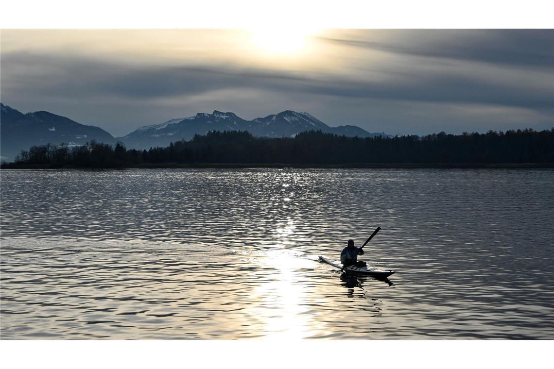 Ein Kajakfahrer fährt vor schneebedeckten Bergen über den Chiemsee.