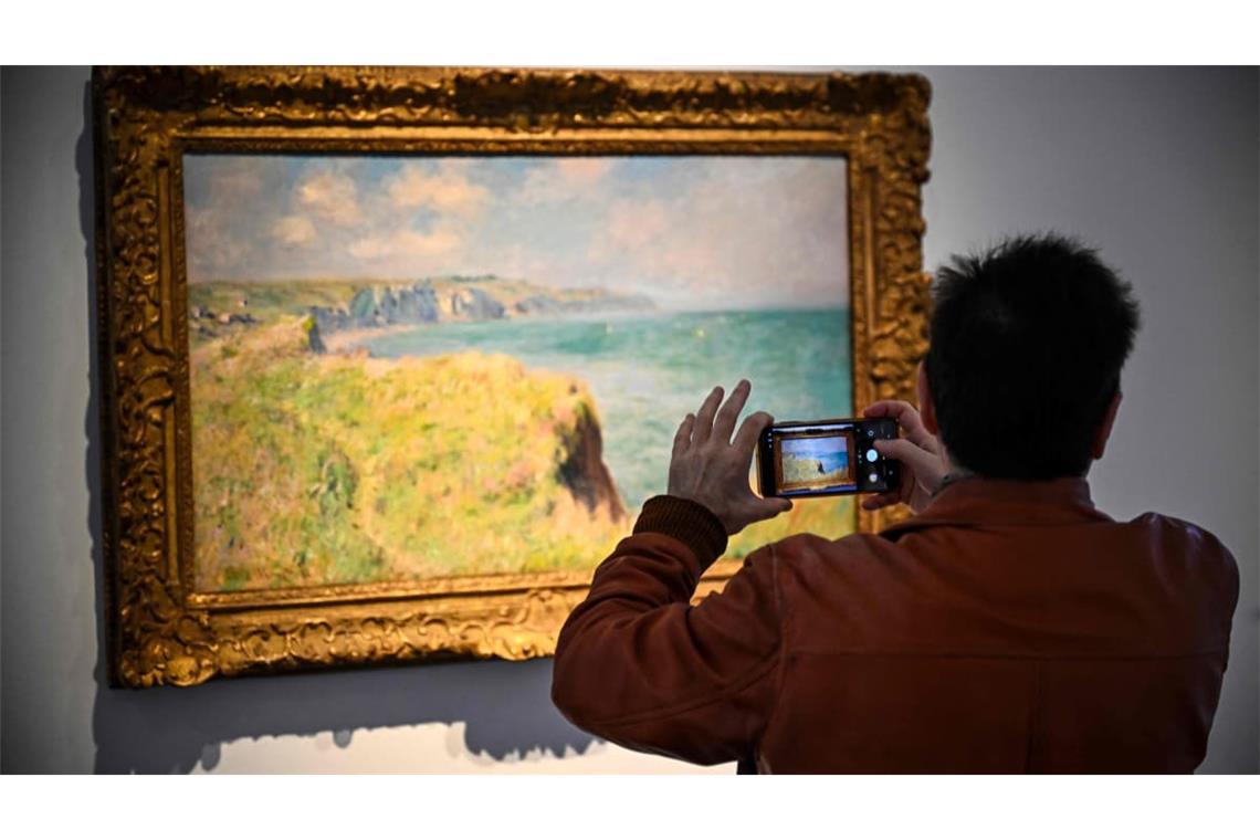 Ein Mann fotografiert ein Gemälde von Claude Monet. Ein zuvor nie öffentlich ausgestelltes Gemälde des Malers Claude Monet ist in Paris zum Rekordpreis versteigert worden (Symbolfoto).