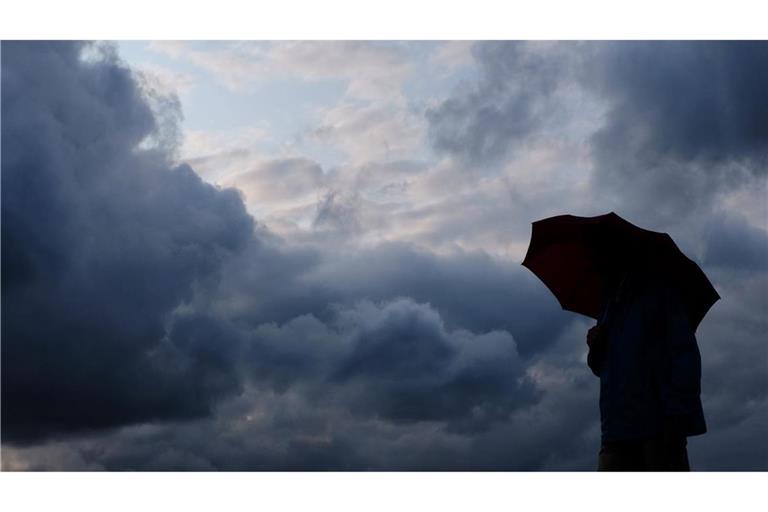 Ein Mann geht mit einem Regenschirm vor aufziehenden dunklen Wolken spazieren. (Symbolbild)