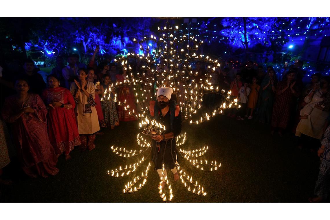 Ein Mann hält in einem mit Öllampen geschmückten Kostüm in der fünften Nacht von Navratri, dem Fest der neun Nächte, das Aarti-Ritual ab.