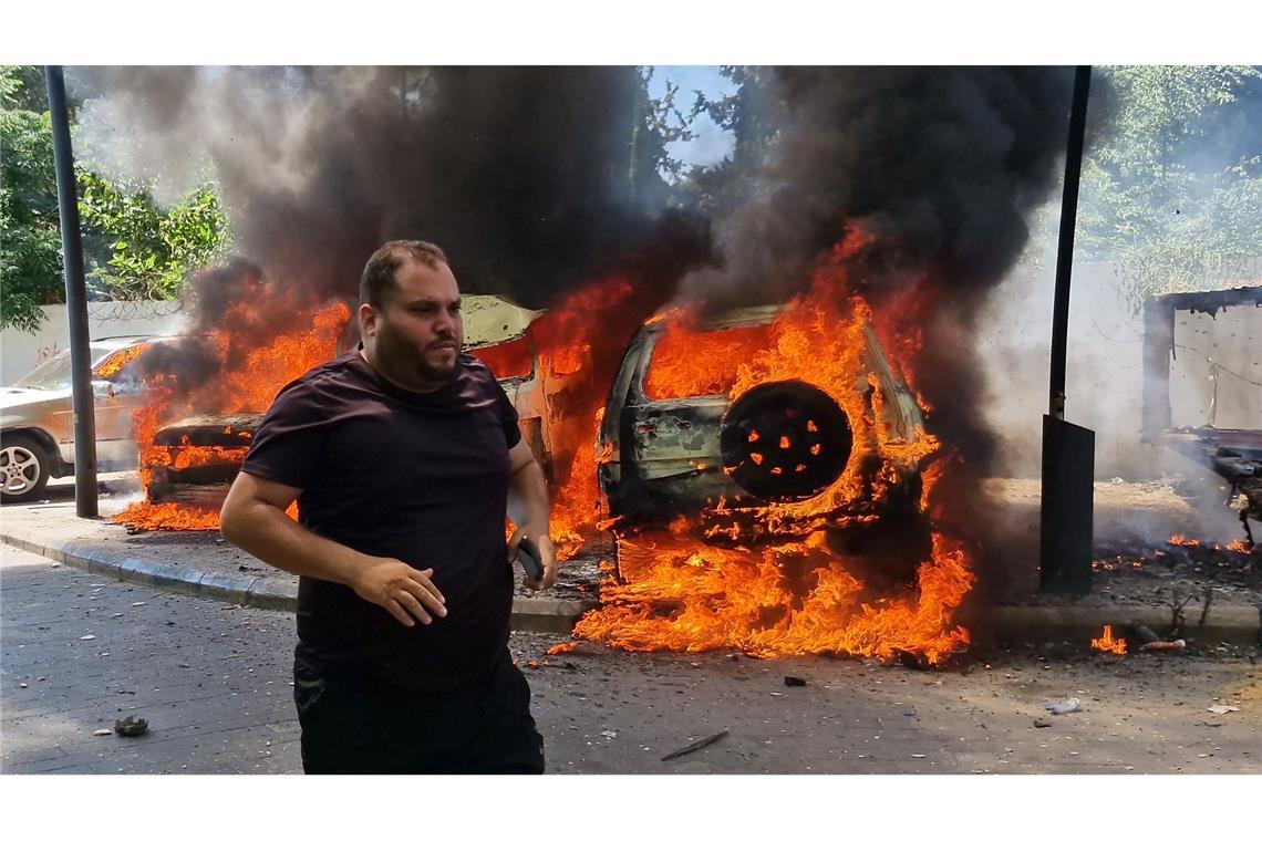 Ein Mann läuft vor brennenden Autos, die bei einem israelischen Luftangriff in der libanesischen Hafenstadt Sidon in Brand geraten sind.