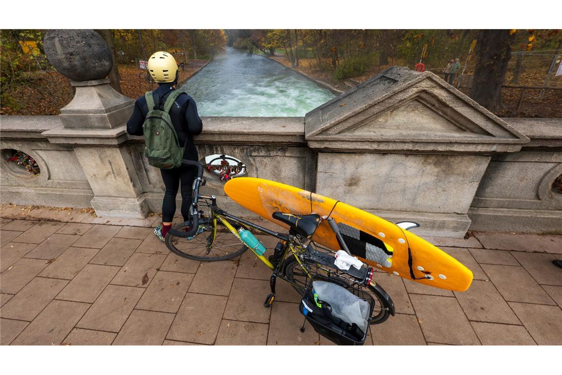 Ein Mann mit einem Surfboard an seinem Fahrrad schaut von einer Brücke auf die - nicht mehr vorhandene - Eisbachwelle im Englischen Garten.