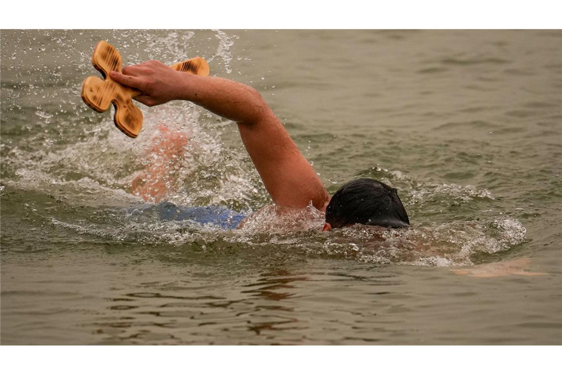 Ein Mann schwimmt mit einem von drei Holzkreuzen, die der orthodoxe Erzbischof Teodosie bei Harsova in die Donau geworfen hat, damit die Menschen sie zurückholen können, während eines Gottesdienstes einen Tag vor dem Dreikönigsfest.