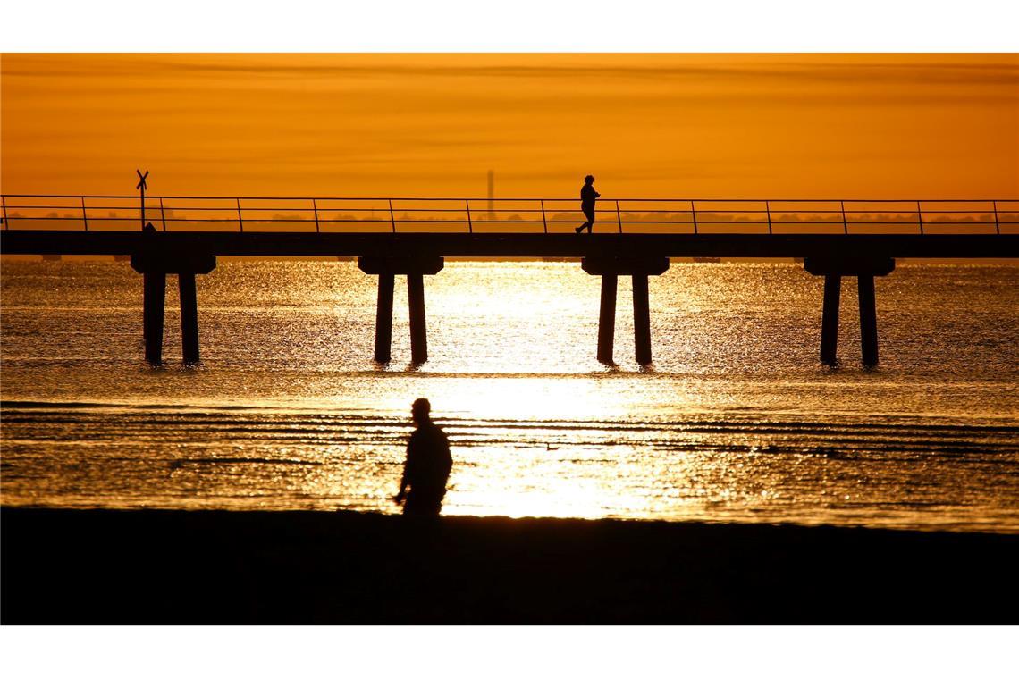 Ein Mann spaziert bei Sonnenaufgang am Altona Pier entlang.