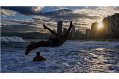 Ein Mann springt bei Temperaturen um die 10 Grad Celsius ins Mittelmeer, während die Sonne über Beirut aufgeht.