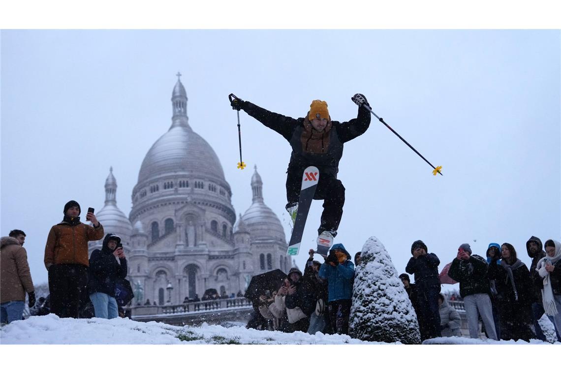 Ein Mann springt mit seinen Skiern den Hügel bei der Basilika Sacre-Coeur hinunter, während es im Viertel Montmartre schneit.