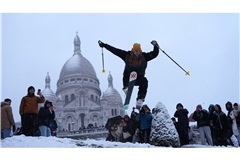 Ein Mann springt mit seinen Skiern den Hügel bei der Basilika Sacre-Coeur hinunter, während es im Viertel Montmartre schneit.