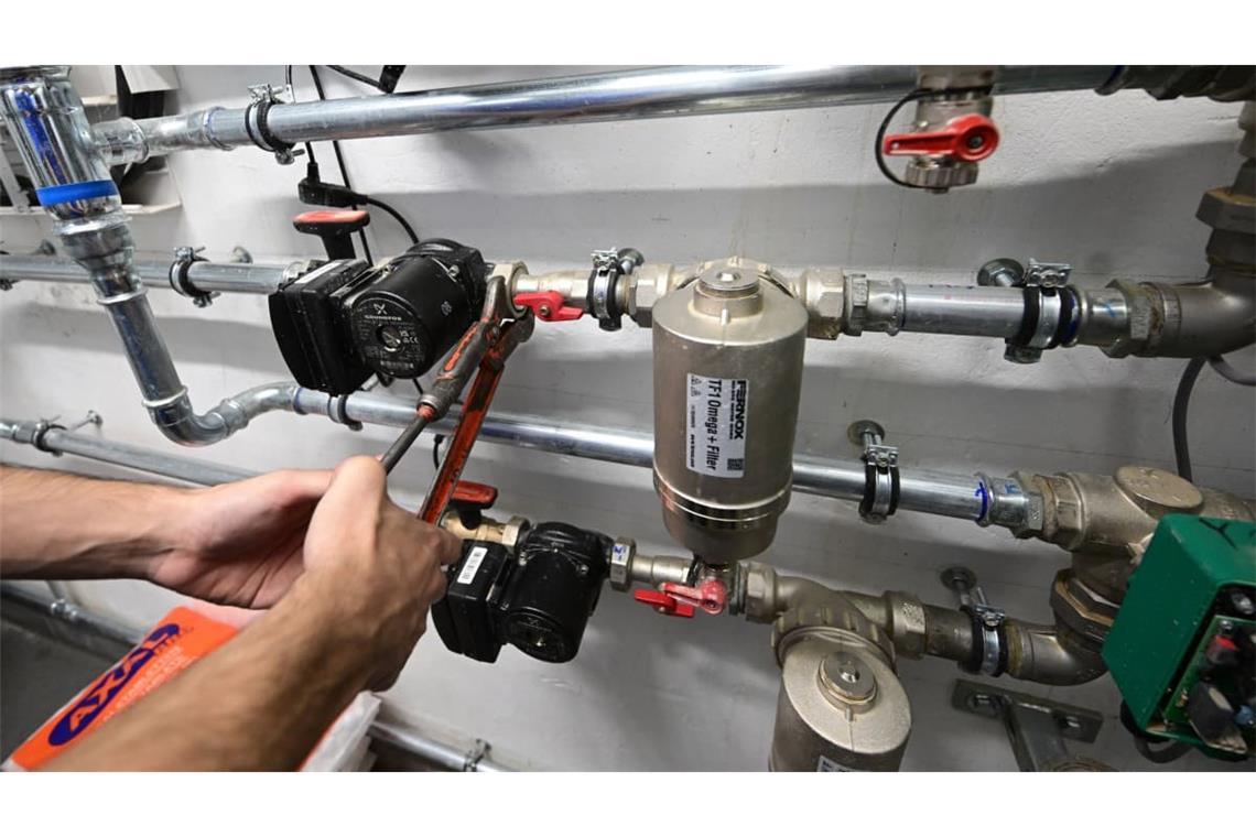 Ein Mitarbeiter eines Handwerksbetriebs arbeitet in einem Heizungskeller an der Installation der Technik für eine Wärmepumpe.