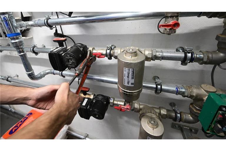 Ein Mitarbeiter eines Handwerksbetriebs arbeitet in einem Heizungskeller an der Installation der Technik für eine Wärmepumpe.