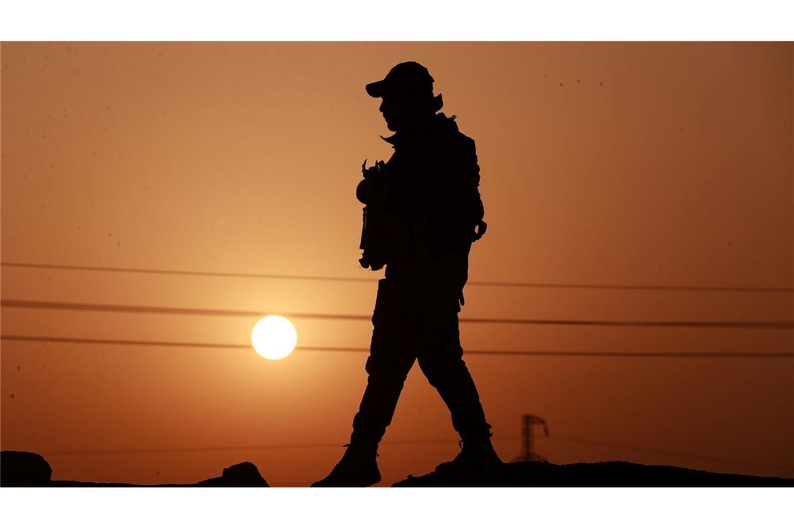 Ein Mitglied der Popular Mobilization Forces läuft an einer Betonmauer entlang.