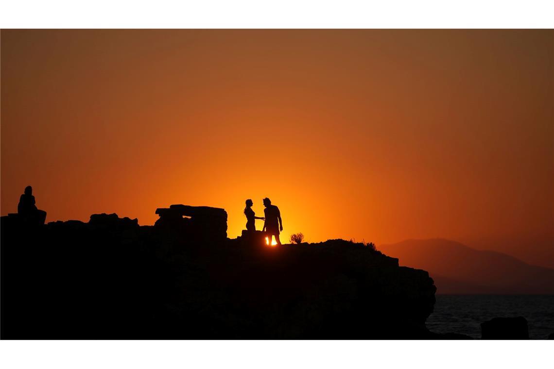 Bilder des Tages Ein Paar steht auf einem Meeresfelsen, während die Sonne an einem warmen und windigen Tag am Strand von Kavouri im Süden Athens untergeht,