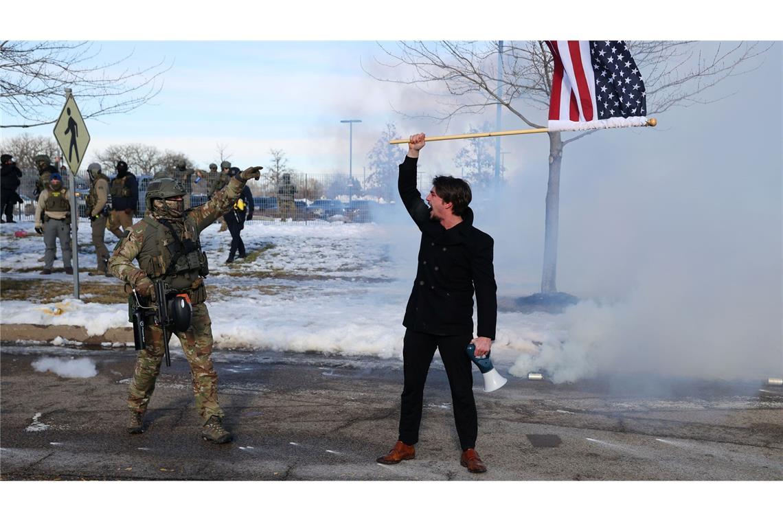 Ein Protestierender mit einer amerikanischen Flagge steht einem ICE-Beamten gegenüber.