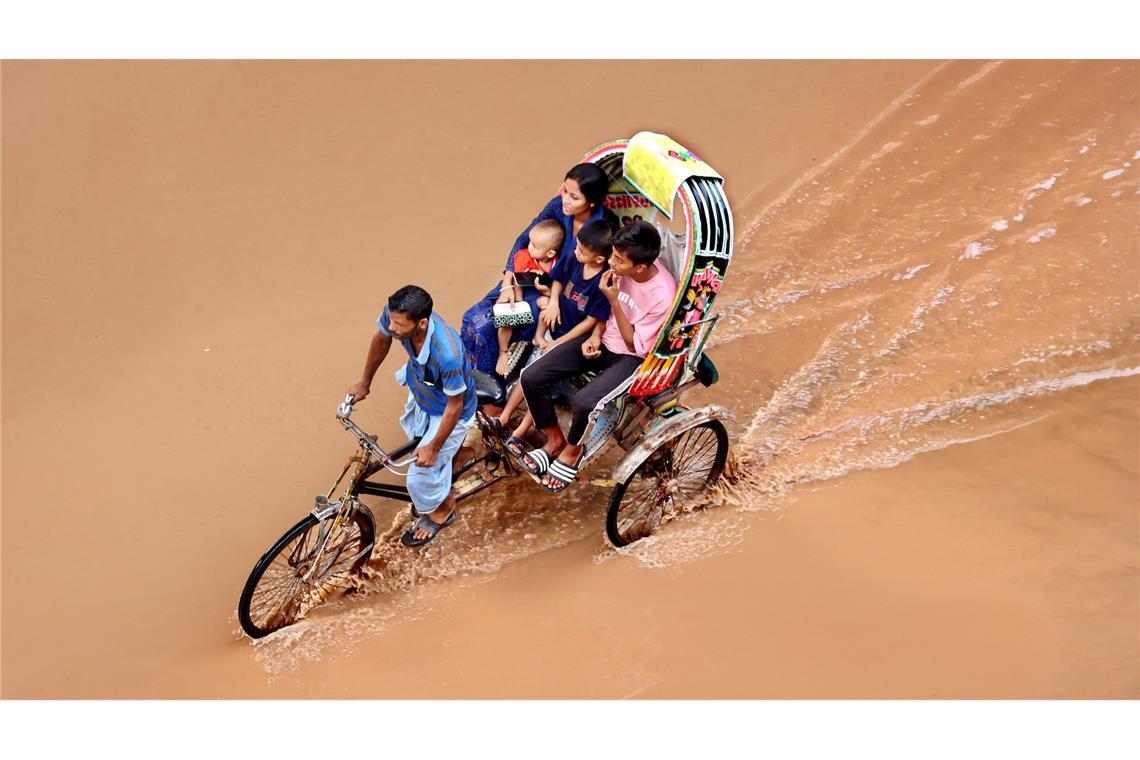 Bilder des Tages Ein Rikschafahrer fährt seine Kunden durch das braune Wasser auf einer überschwemmten Straße in Chittagong in Bangladesch.