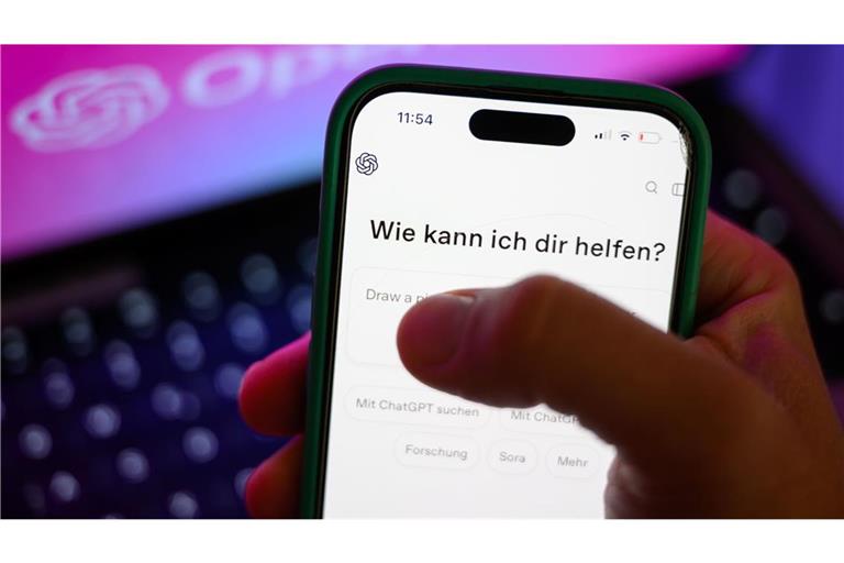 Ein Smartphone mit dem KI-Chatbot ChatGPT ist vor dem Logo des US-Softwareunternehmens OpenAI zu sehen. Das KI-Unternehmen hat eine Kindersicherung angekündigt (Symbolfoto).